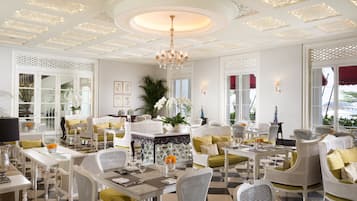 A spacious dining area with white wicker furniture, a central table with a chandelier, and a checkered floor.