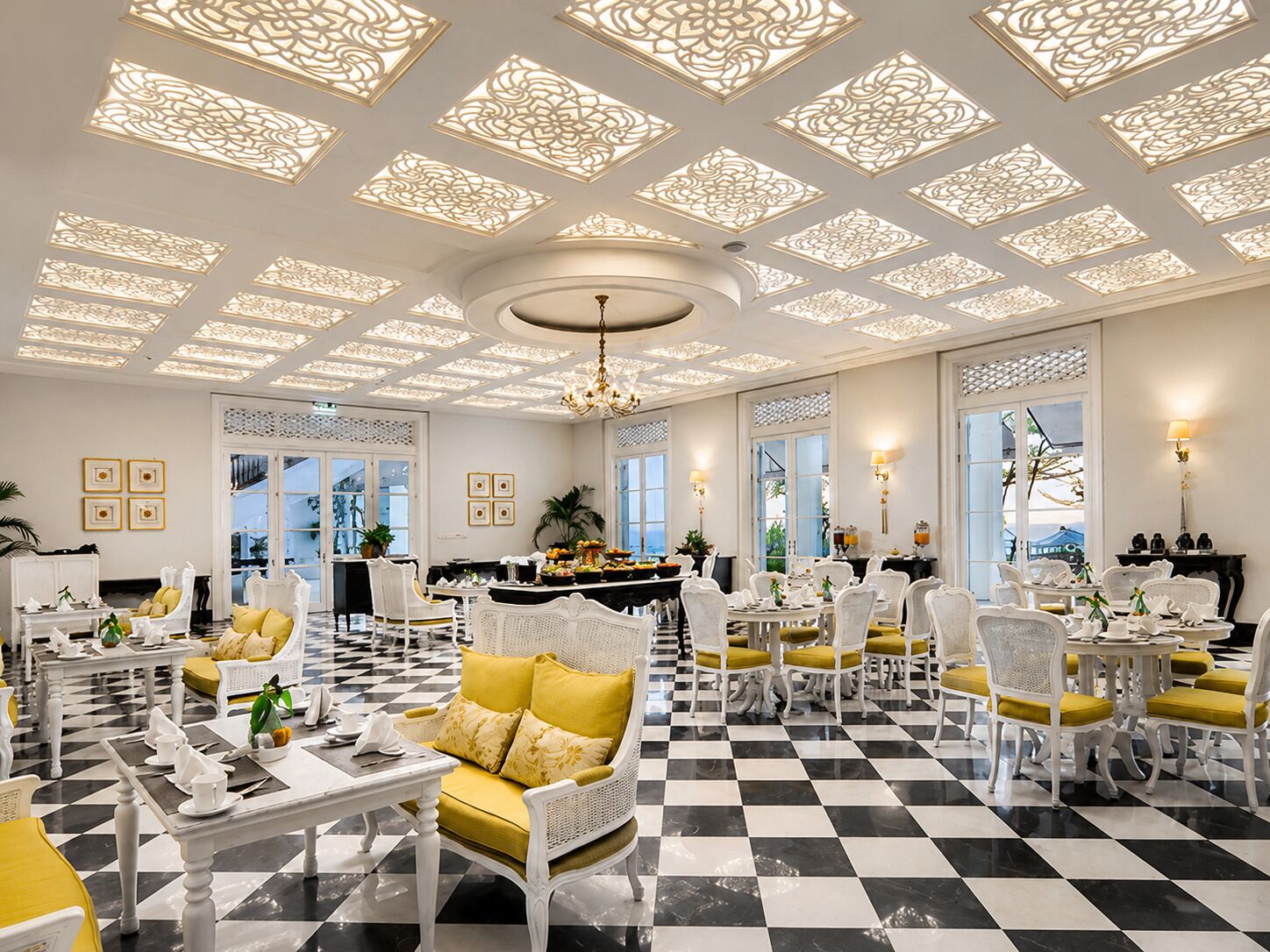 A hotel lobby with a checkered floor, white furniture, and decorative ceiling panels.