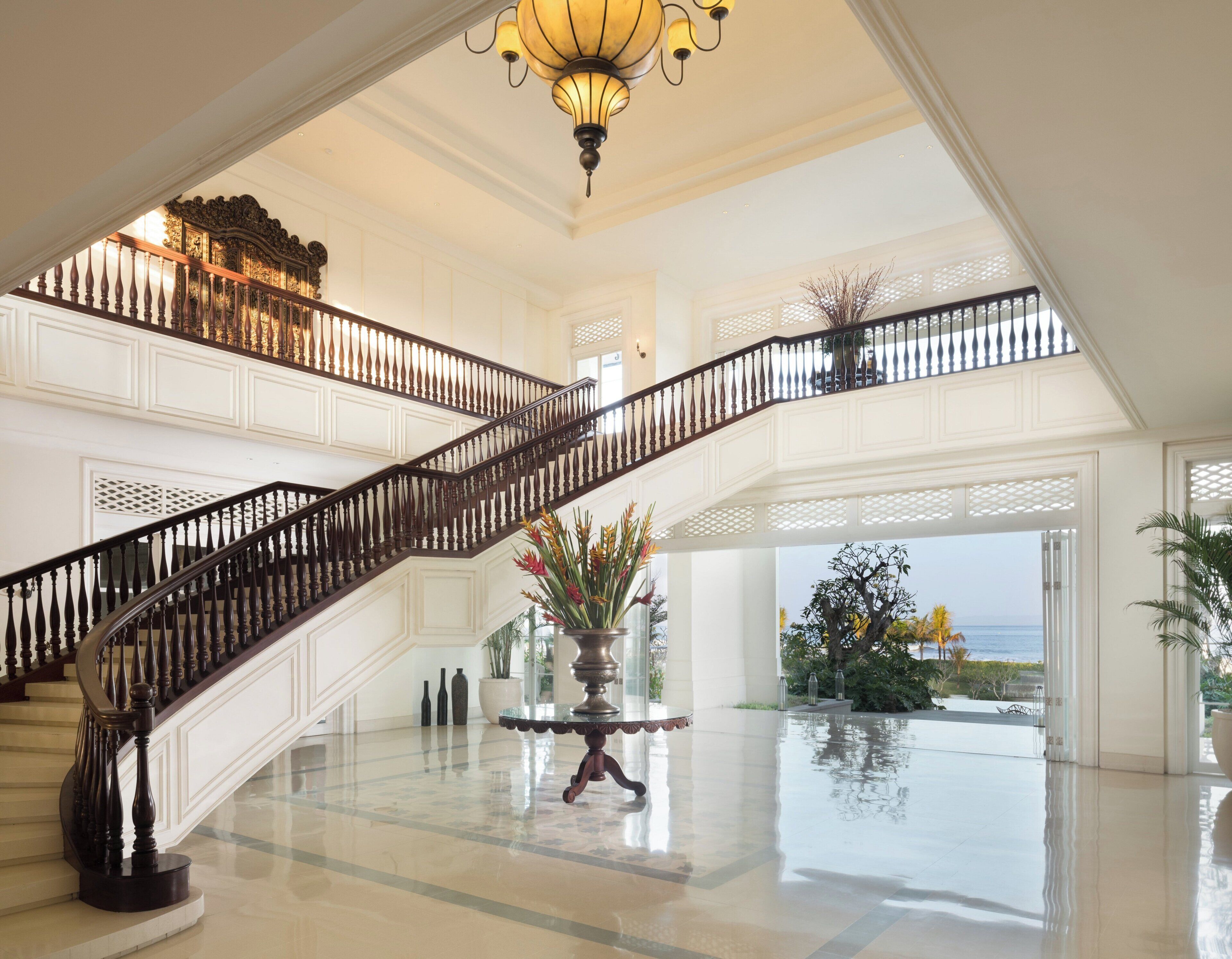 A grand staircase with a balustrade leading to a balcony overlooking a pool and ocean view.