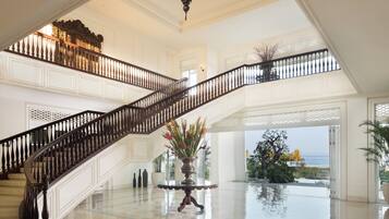 A grand staircase with a balustrade leading to a balcony overlooking a pool and ocean view.