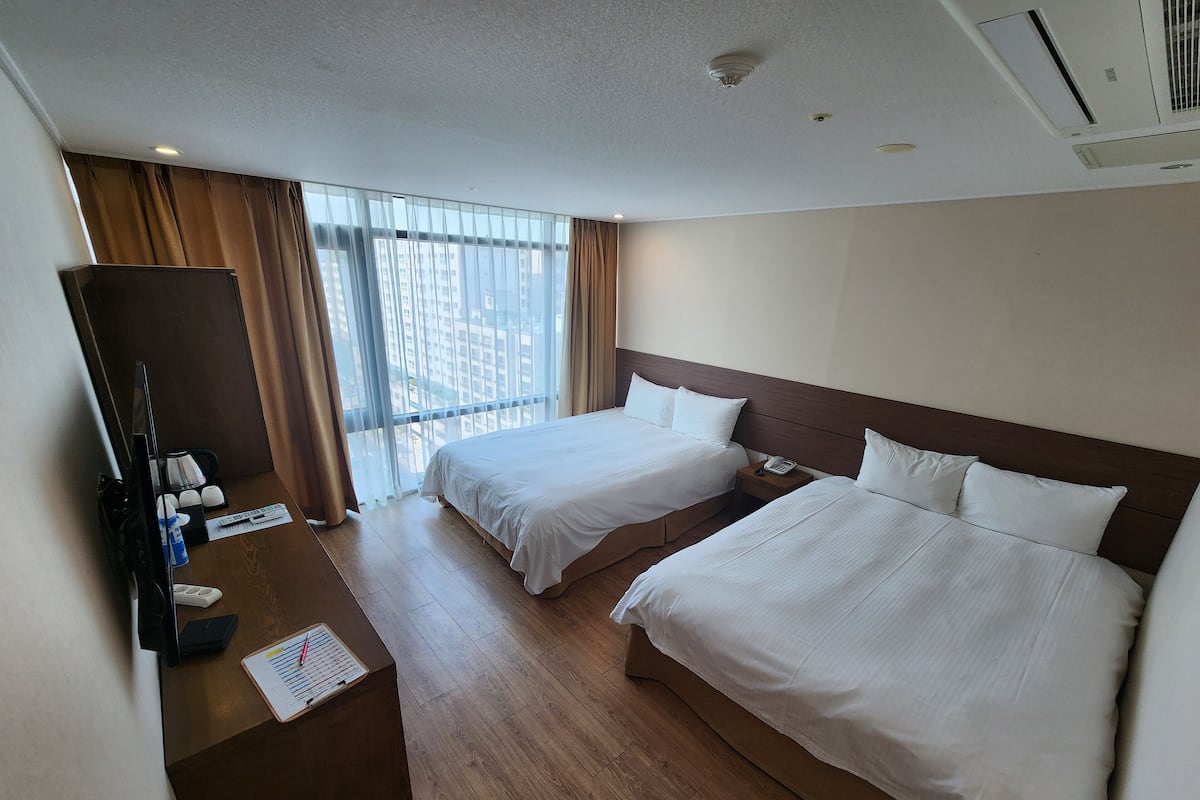 A hotel room with two beds, a desk with a telephone, and a large window with curtains.