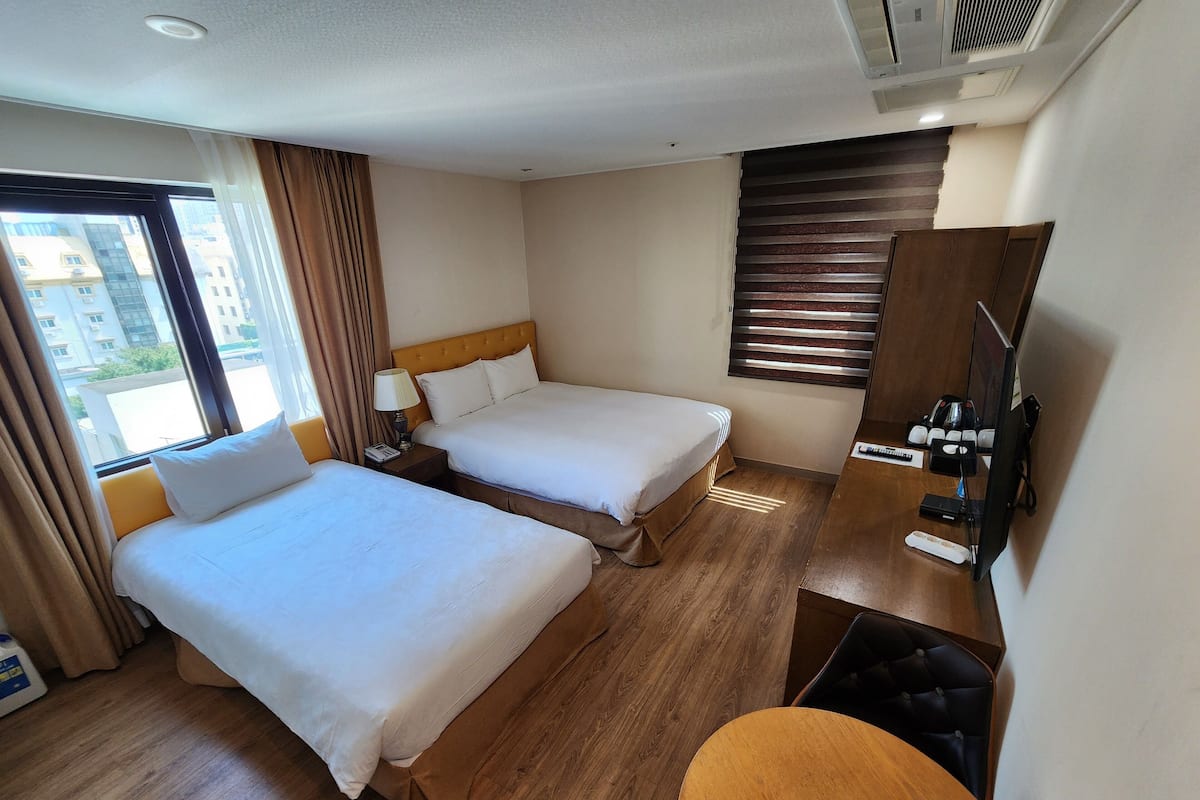 A hotel room with two beds, a desk with a chair, a TV, and a window with curtains.