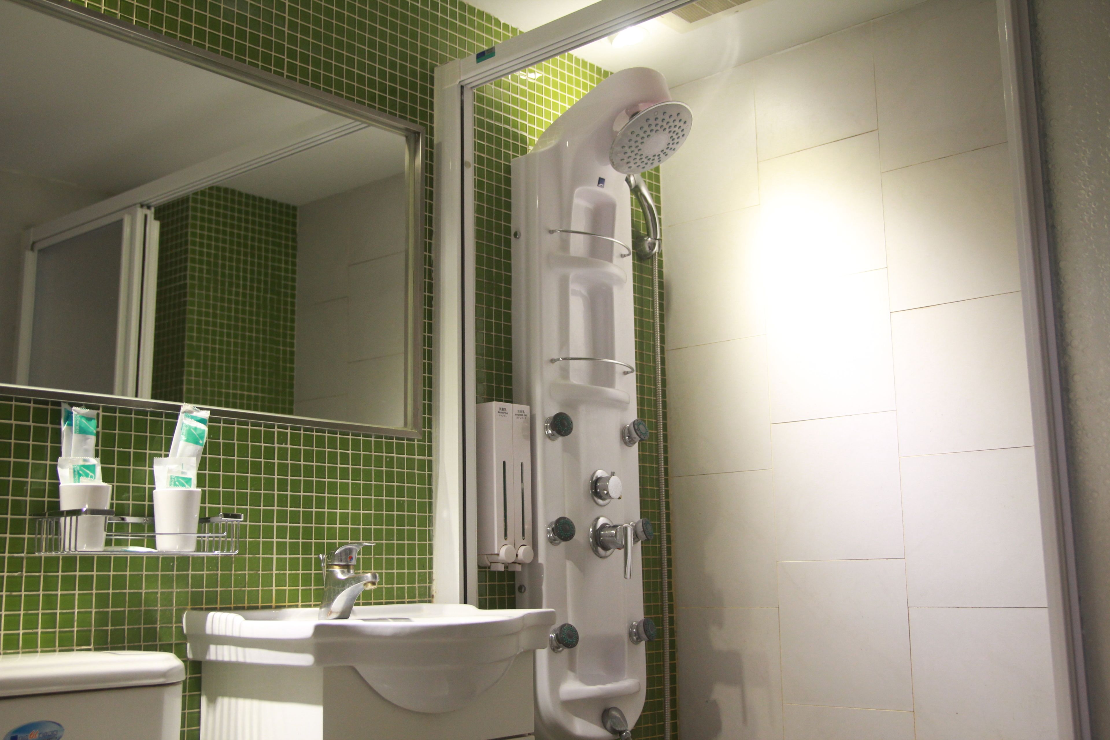 A bathroom with a shower, sink, and green-tiled walls.