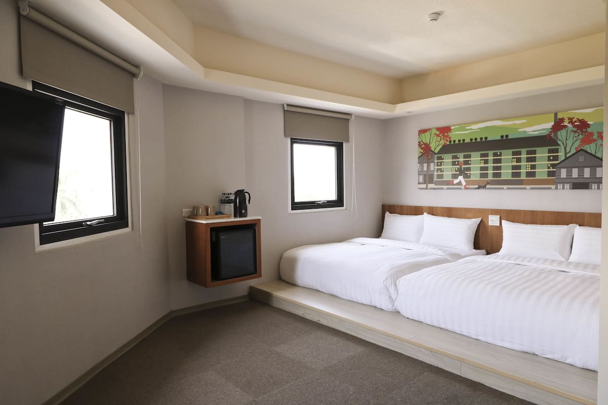 A hotel room with a bed, a TV, a small table with a coffee maker, and a painting on the wall.