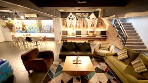 A modern living area with a sofa, armchairs, and a coffee table. There is a staircase and a kitchen area in the background.