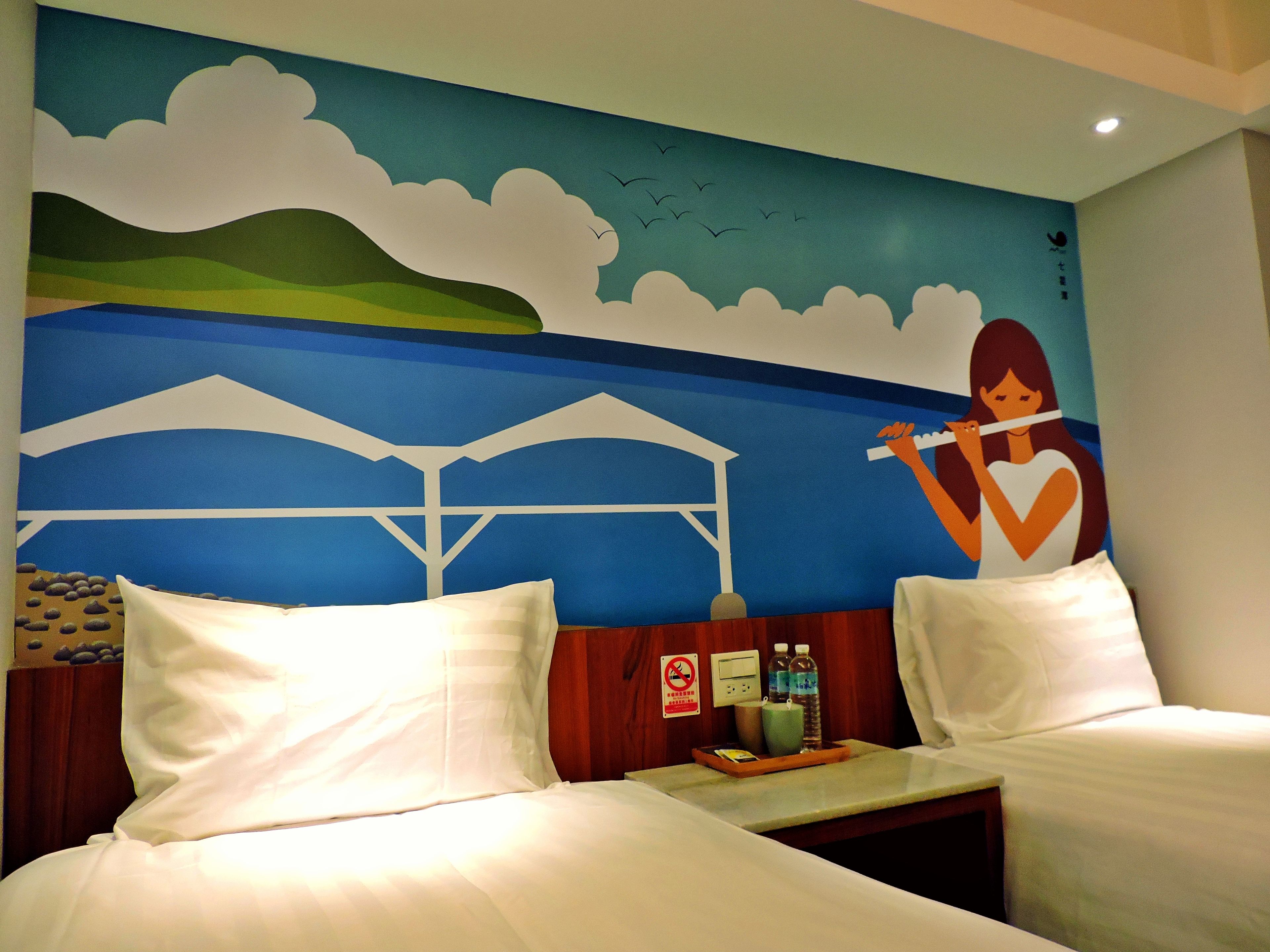 Habitación de hotel con dos camas, un mural en la pared y una mesita con bandeja.