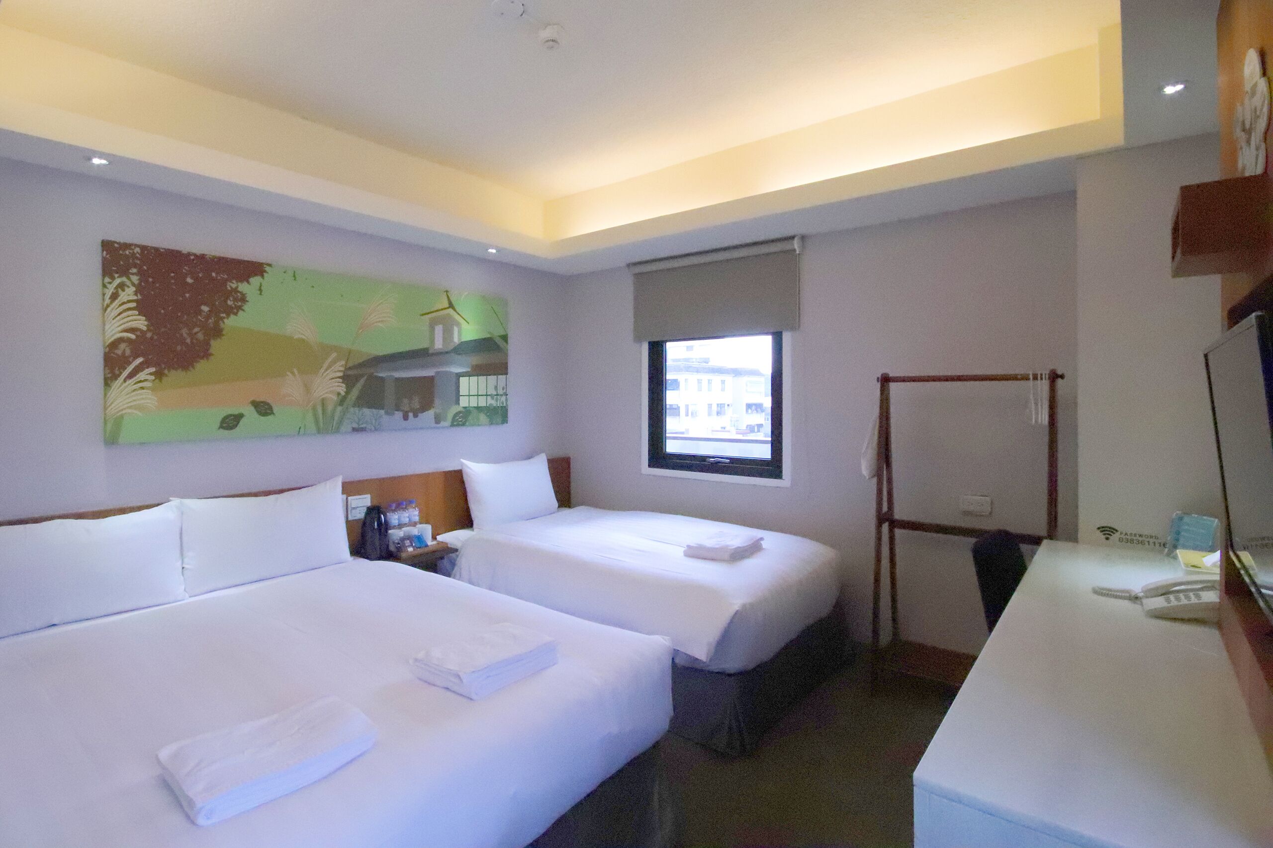 Une chambre d’hôtel avec deux lits, un bureau, une chaise, une fenêtre et un tableau au mur.