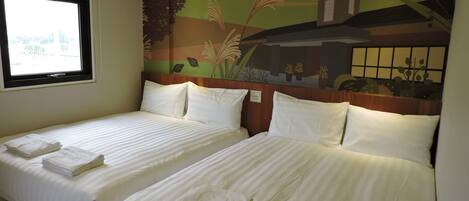 Habitación de hotel con dos camas, cada una con ropa de cama y toallas blancas, una ventana que ofrece vistas a zonas verdes y un mural en la pared que representa un paisaje con un edificio.