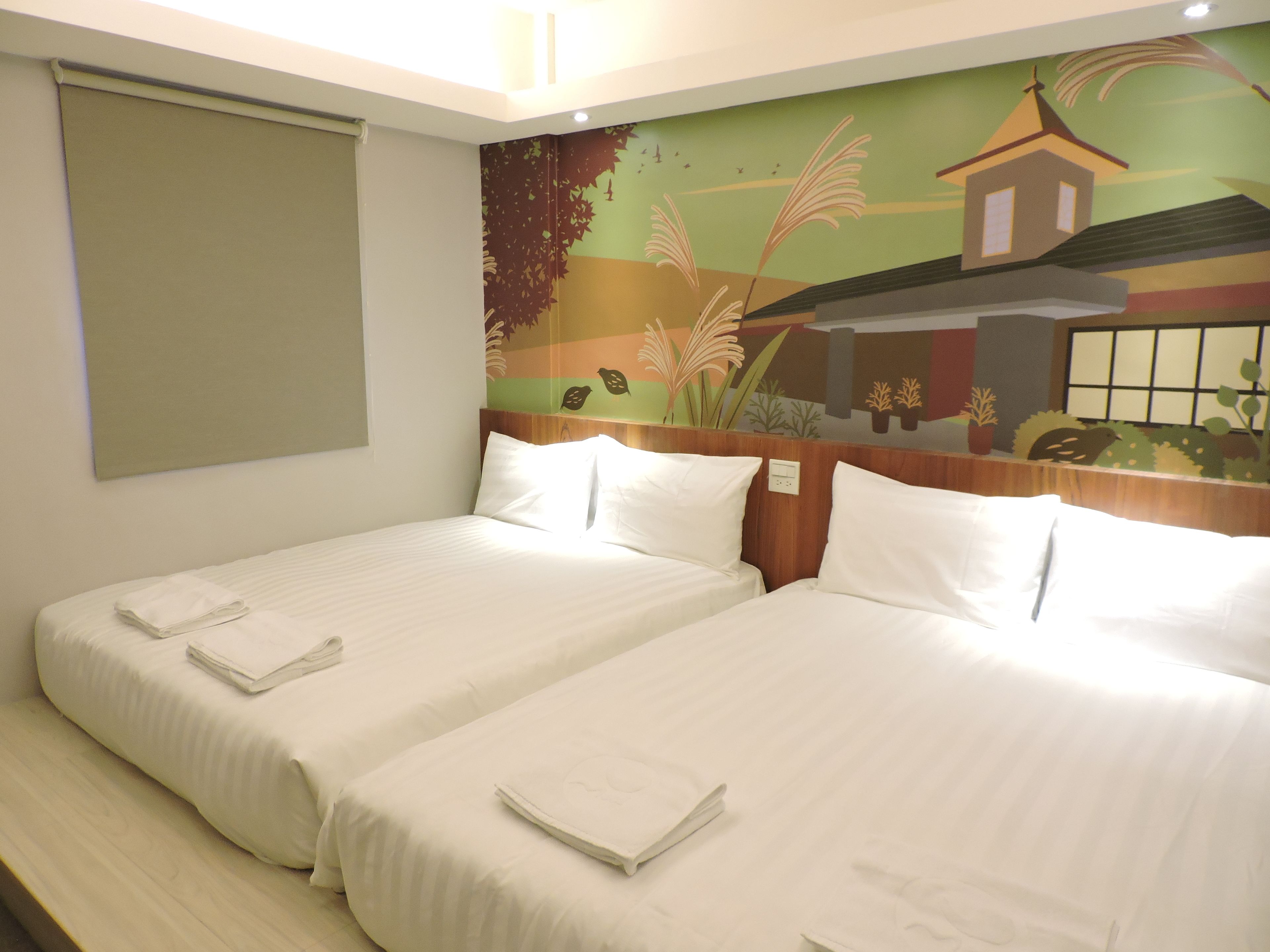 A hotel room with two beds, a mural on the wall, and a window with blinds.
