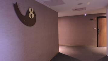 A hallway with a wall-mounted number sign, a door, and a ceiling with recessed lighting and ventilation.