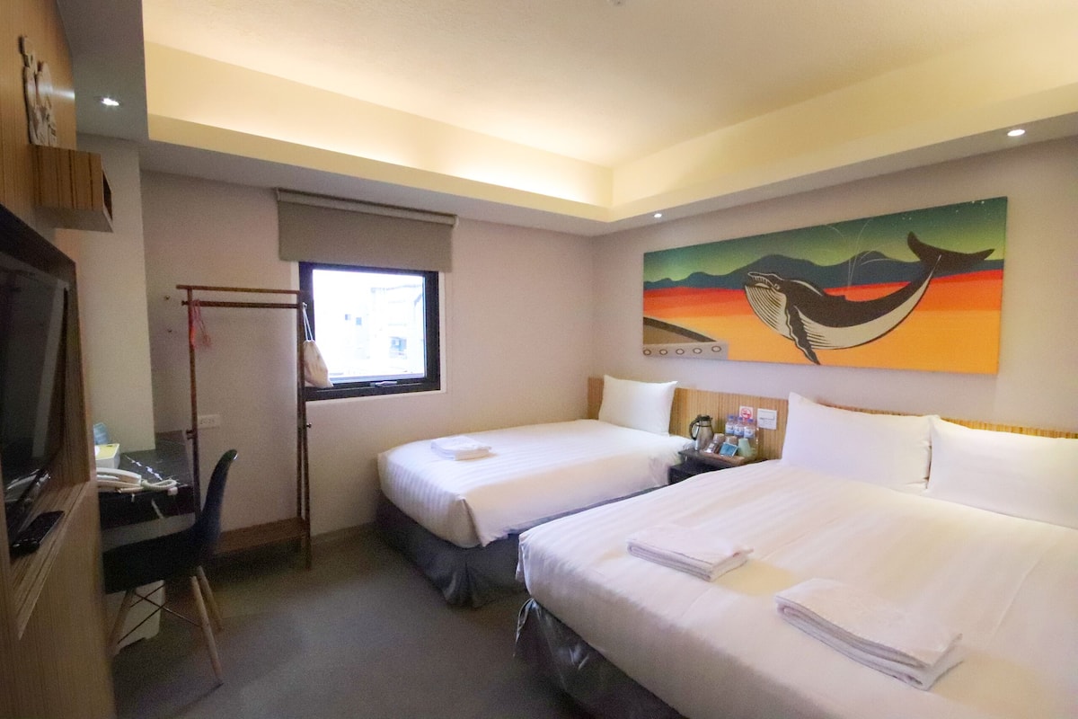A hotel room with two beds, a desk with a chair, a TV, and a painting on the wall.