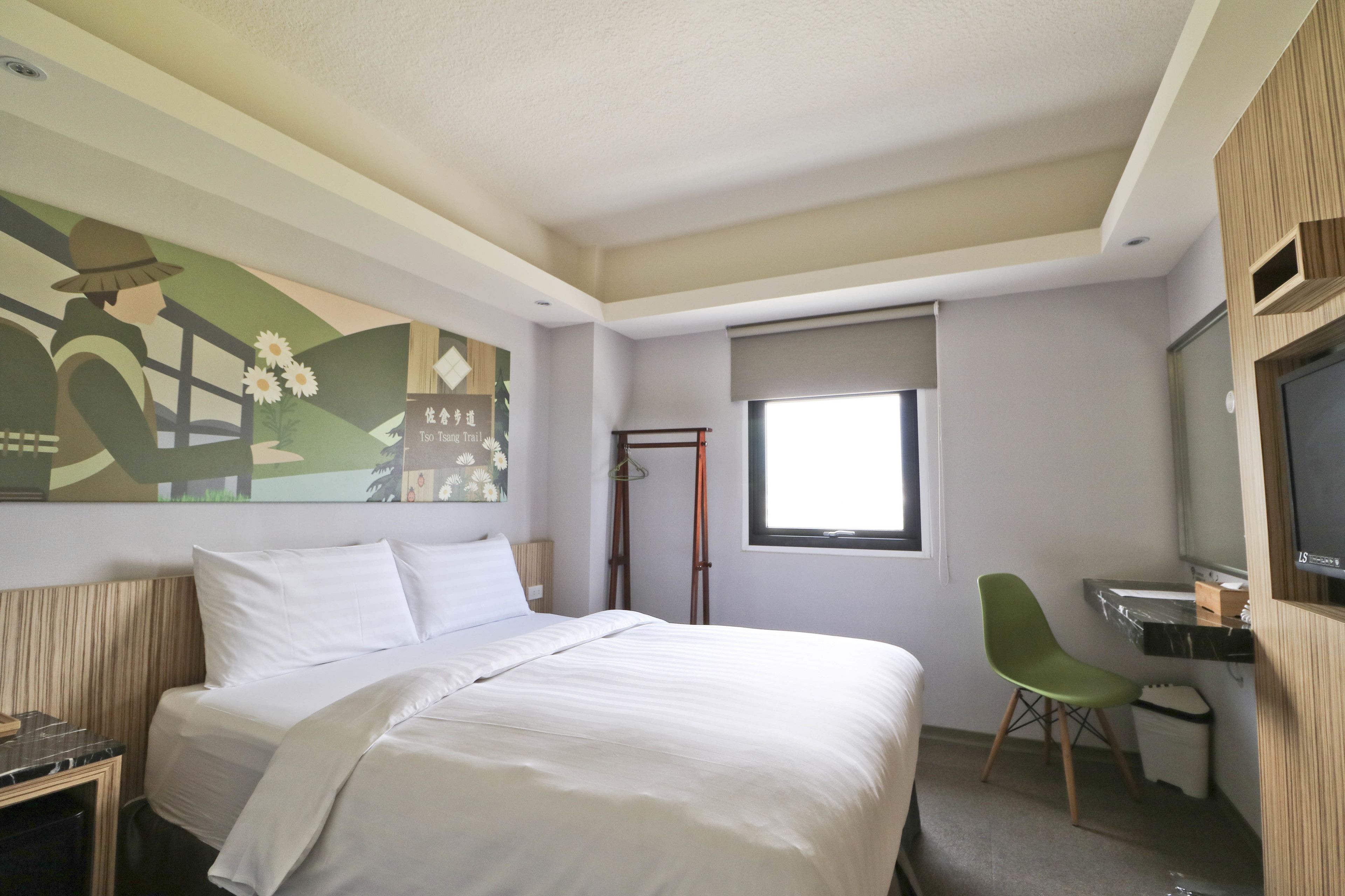 A hotel room with a bed, a desk, a chair, a TV, and a window.