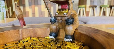 Una escultura de madera de una rana sosteniendo un malanga, rodeada de monedas de oro.