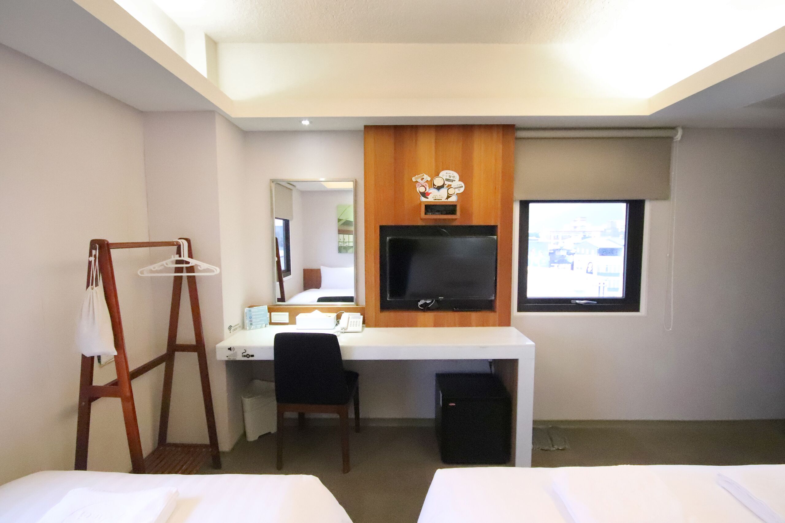 A hotel room with a desk, chair, television, and two beds.