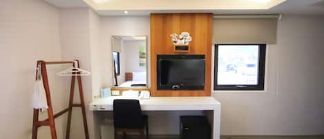 A hotel room with a desk, chair, television, and two beds.