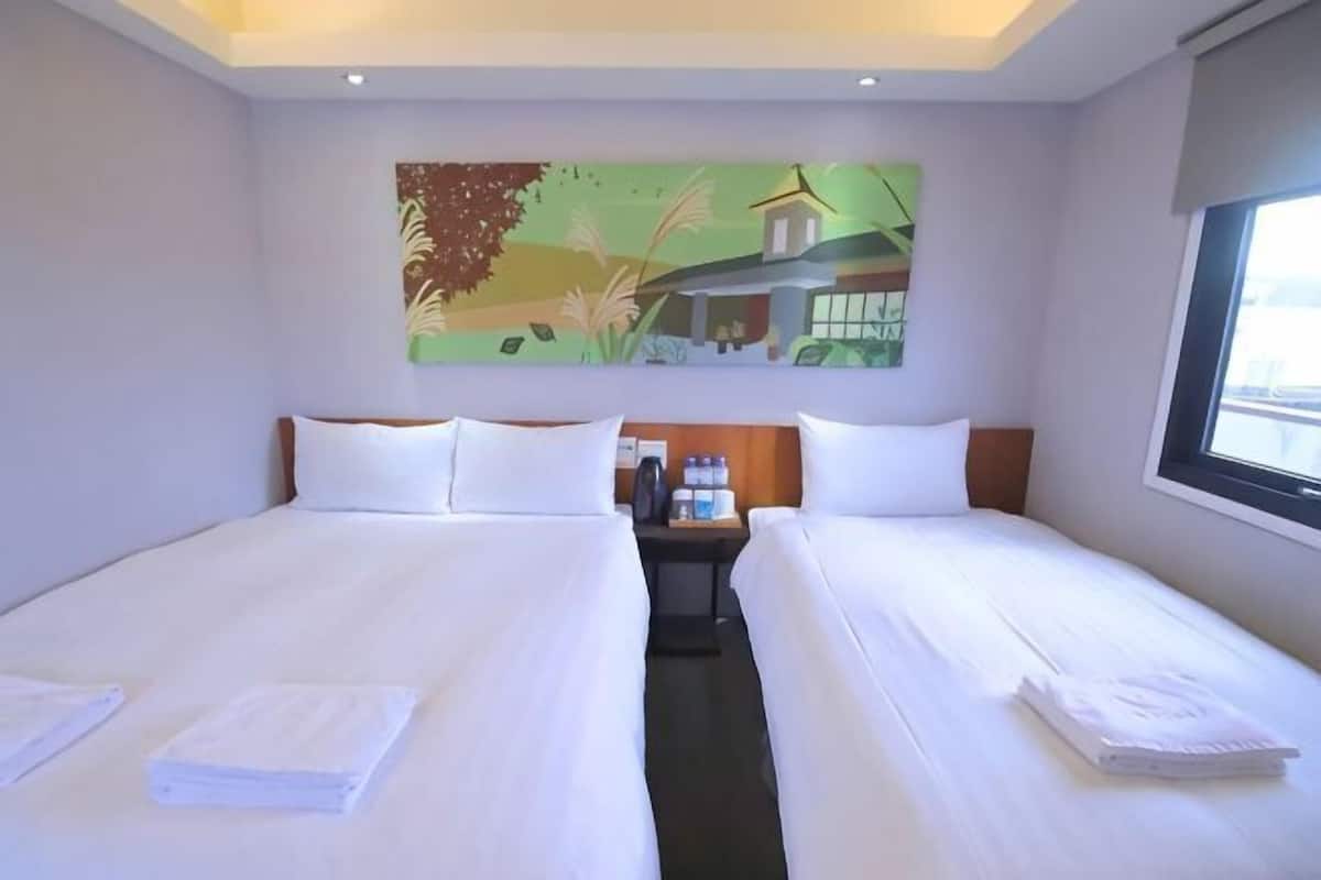 A hotel room with two beds, a nightstand, a painting, and a window.