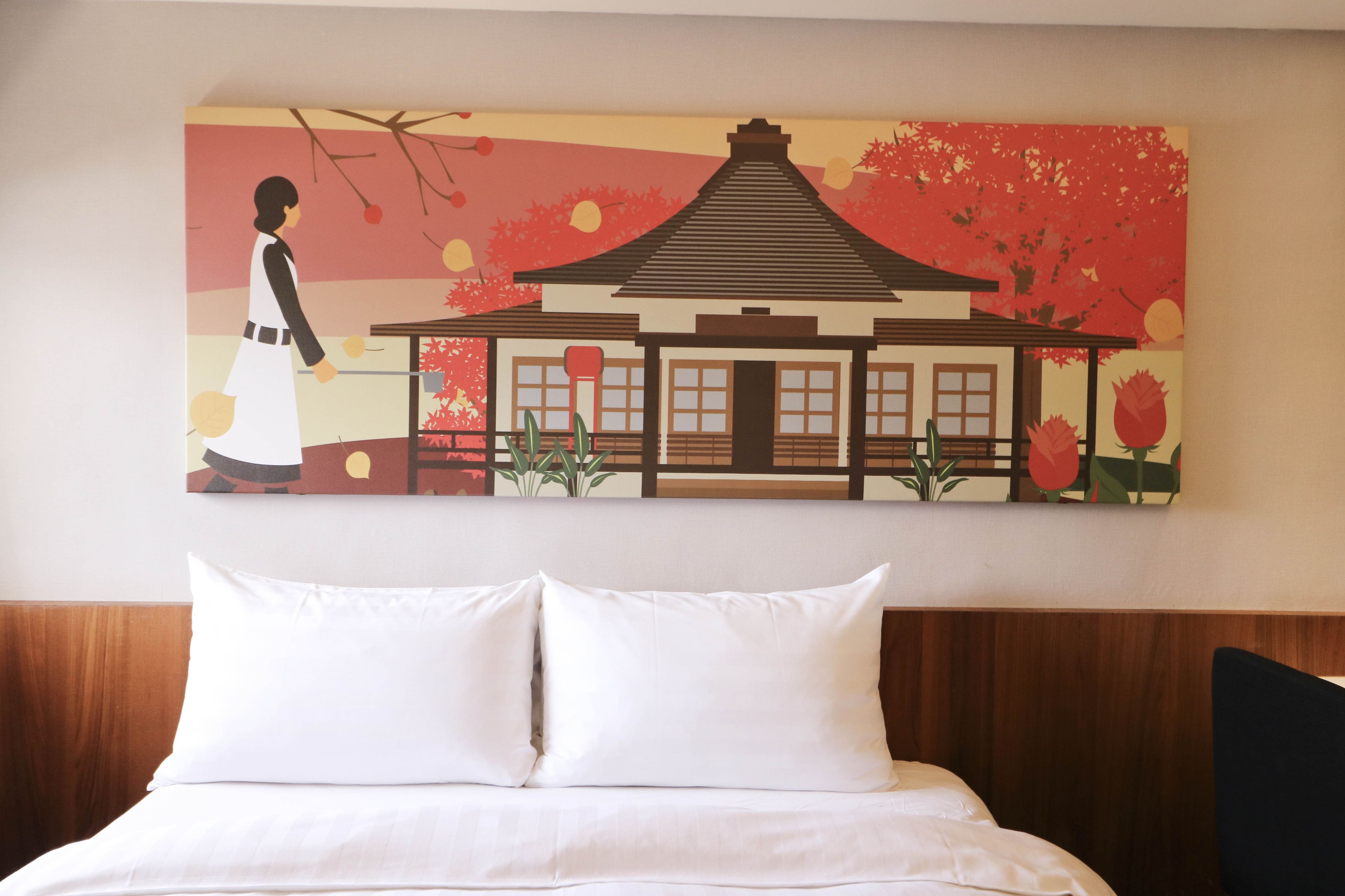Una habitación de hotel con una cama, almohadas blancas y un cuadro colgado en la pared que muestra un edificio tradicional.