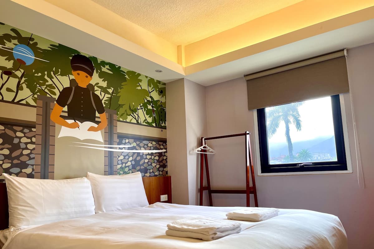 A neatly made bed with white linens and towels, a window with a view of palm trees, and a wall mural of a person with a bird.