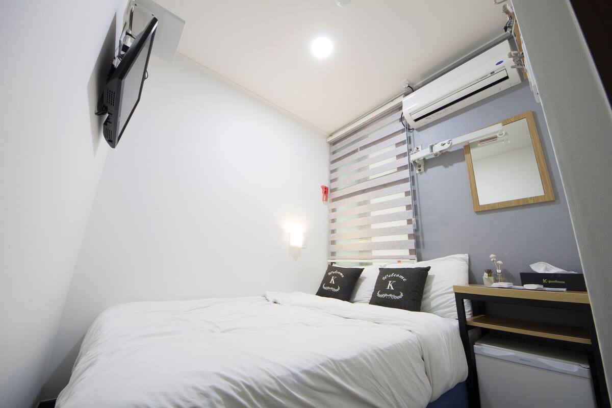 Een slaapkamer met een bed, nachtkastje, spiegel en raam met zonwering.