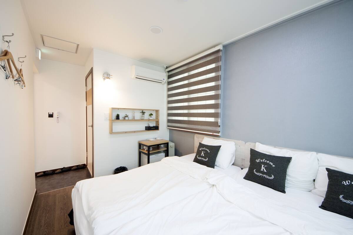 Een slaapkamer met een groot bed, nachtkastje, spiegel en een raam met zonwering.