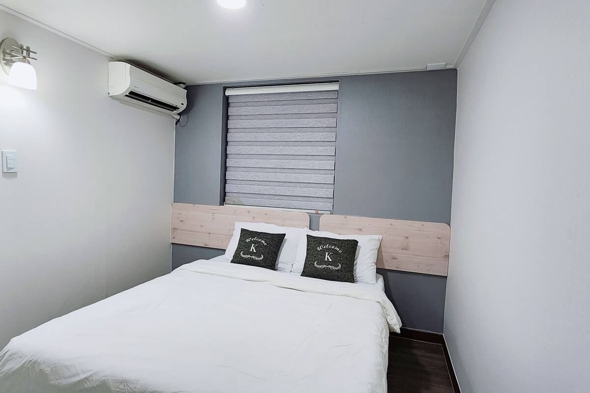 Een compacte, verzorgde slaapkamer met een eenpersoonsbed, een raam met zonwering, een airconditioning en een deur.
