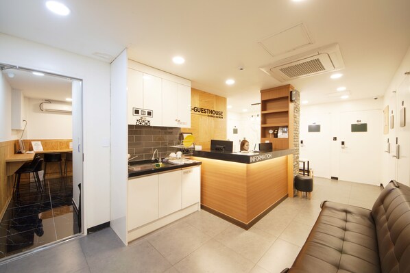 A modern hotel lobby with a reception desk, a seating area, and a kitchenette.