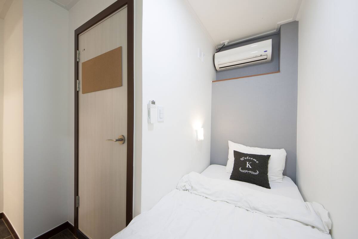 Een hotelkamer met een bed, een deur, een airconditioner en een welkomstkussen.