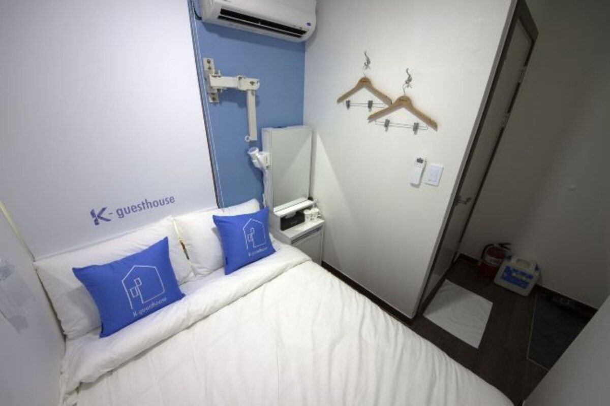 Habitación de hotel con cama, mesita de noche, espejo, armario y aire acondicionado instalado en la pared.