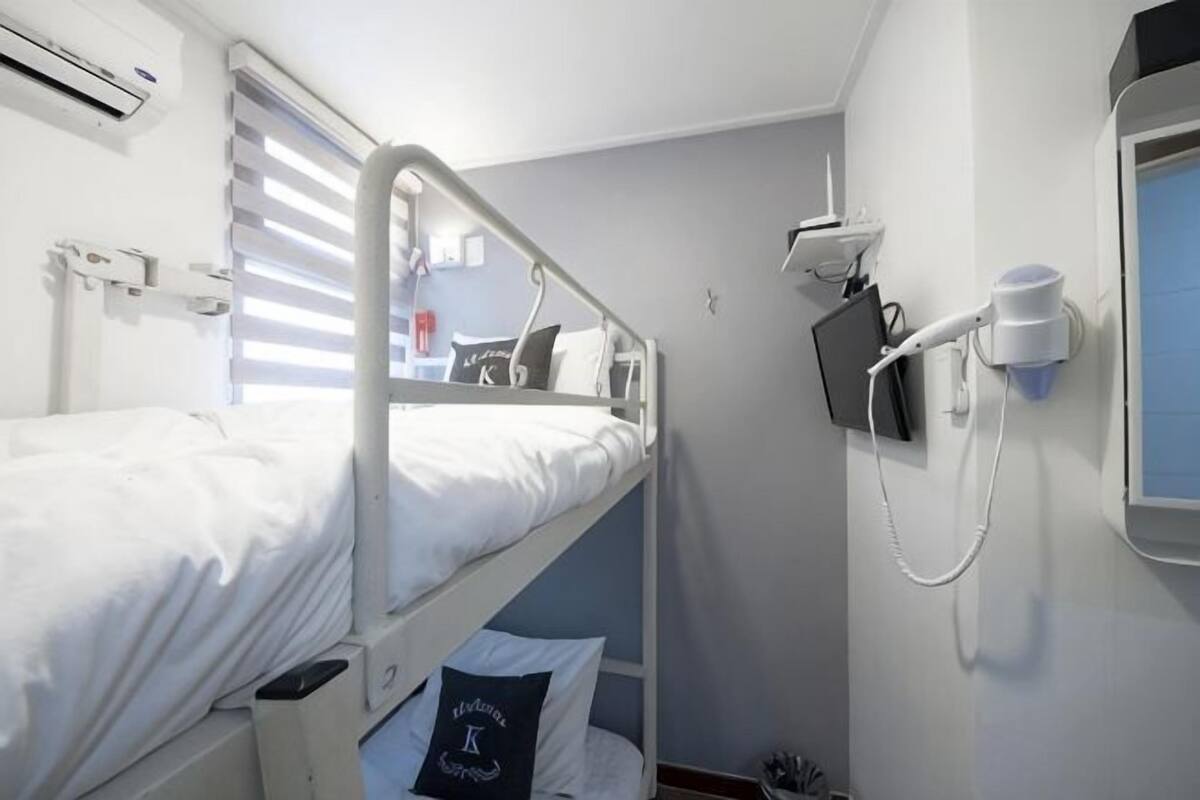 Een slaapkamer met stapelbed, een raam, een bureau en een aan de muur bevestigd telefoon.