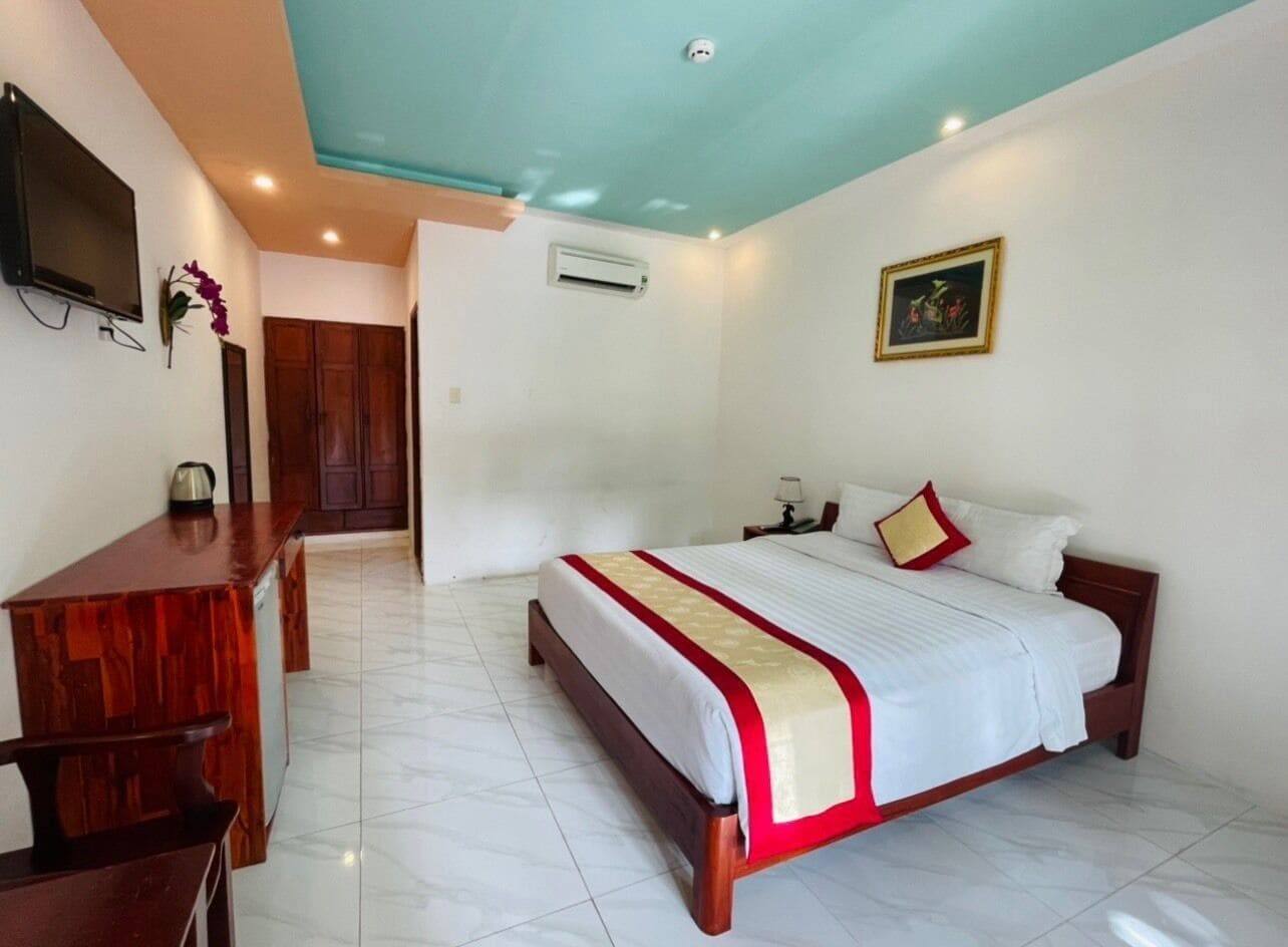 A hotel room with a bed, a desk, a television, and an air conditioning unit.