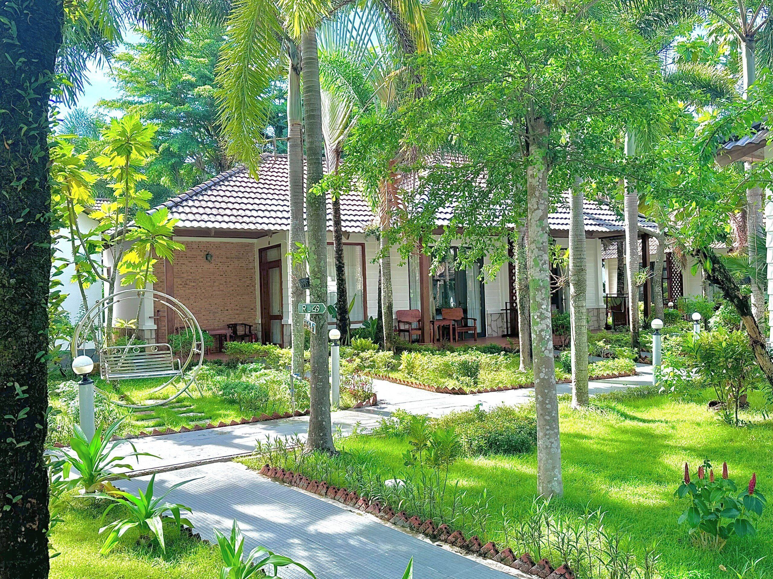 A residential area with a house featuring a tiled roof, a porch with seating, and a well-maintained garden with various plants and a pathway.