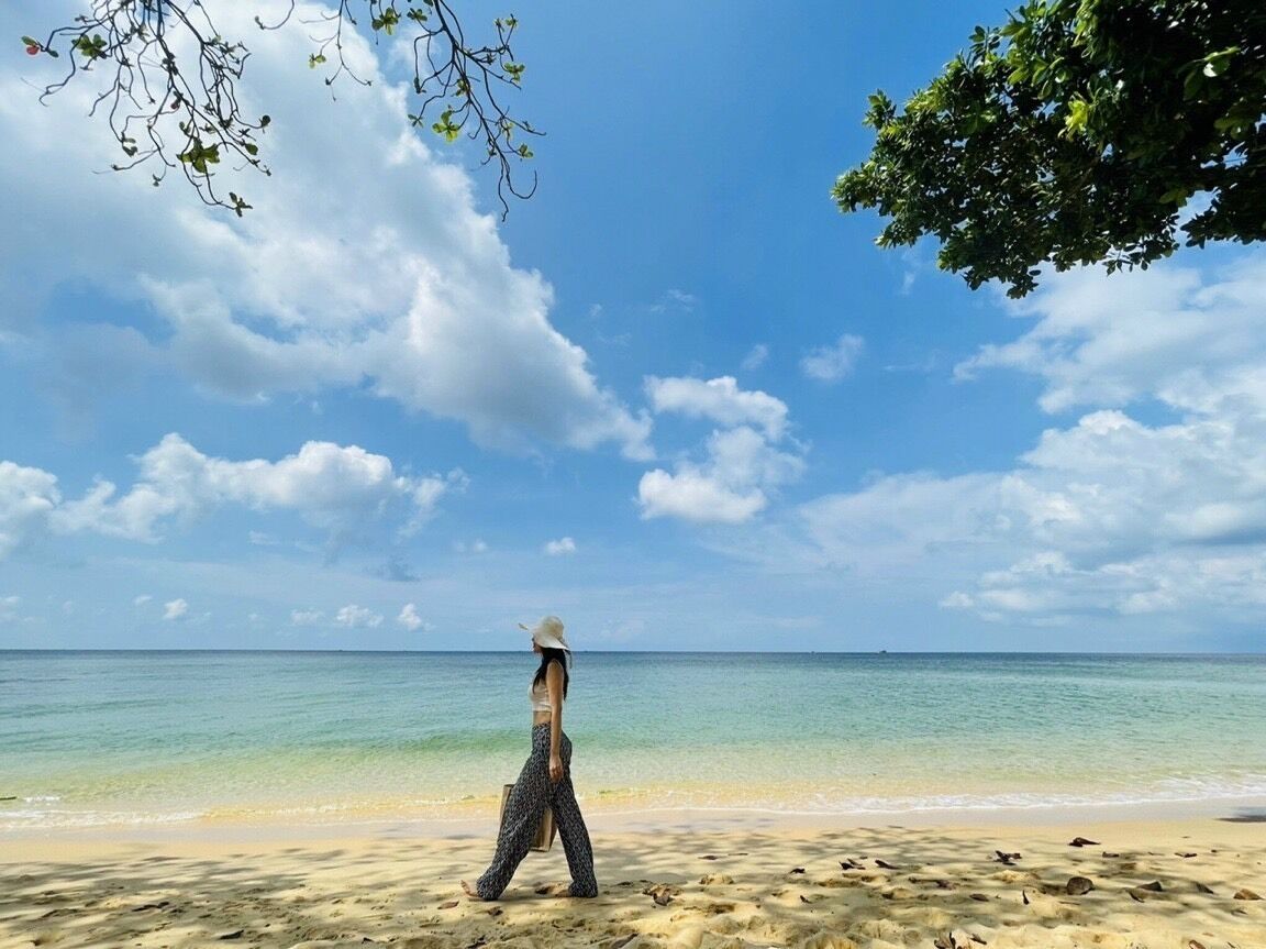 Una persona caminando sobre una playa arenosa con cielos despejados y agua tranquila.