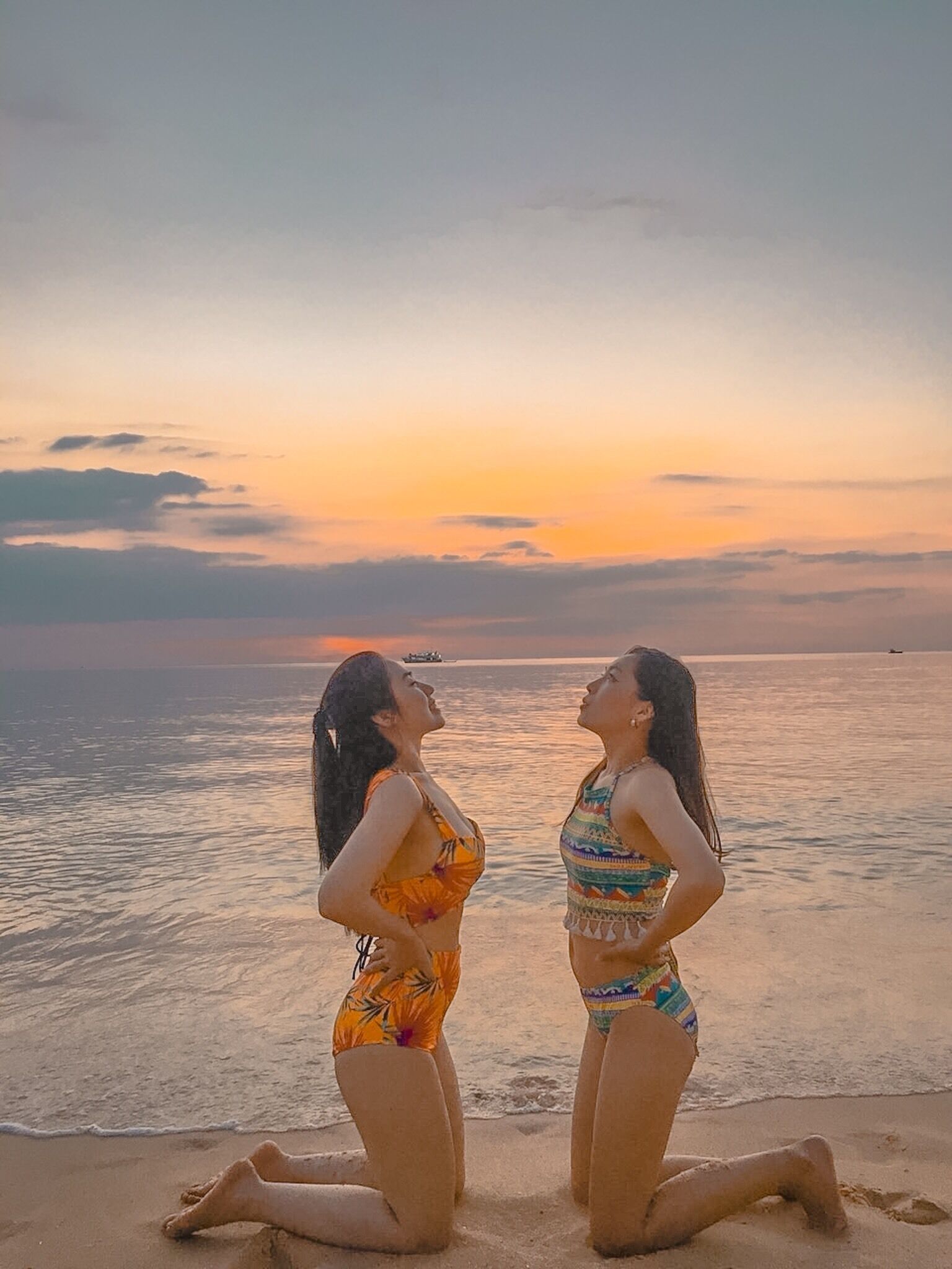 Two women kneeling on a beach at sunset.