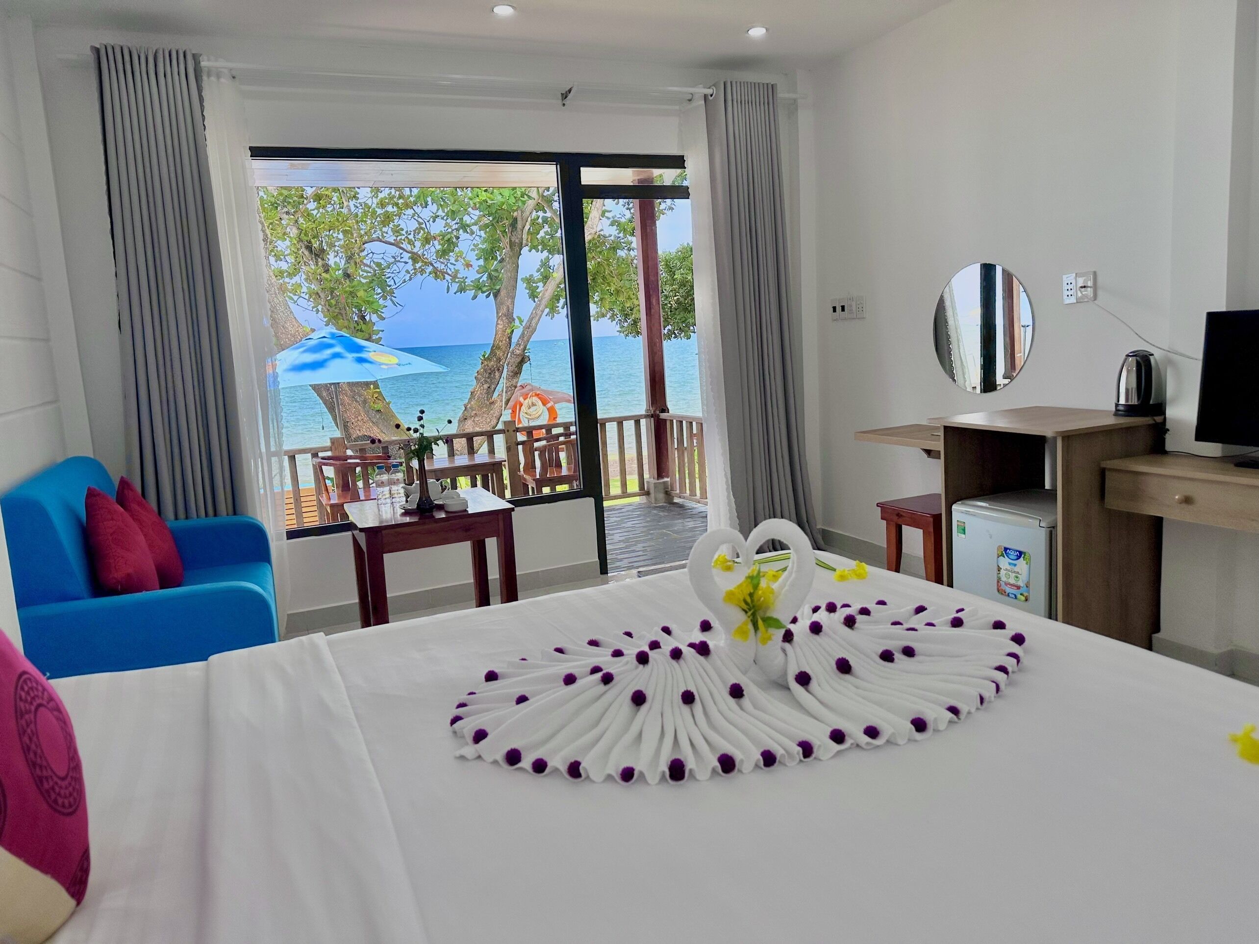 A hotel room with a bed, a desk, a television, and a view of the sea.