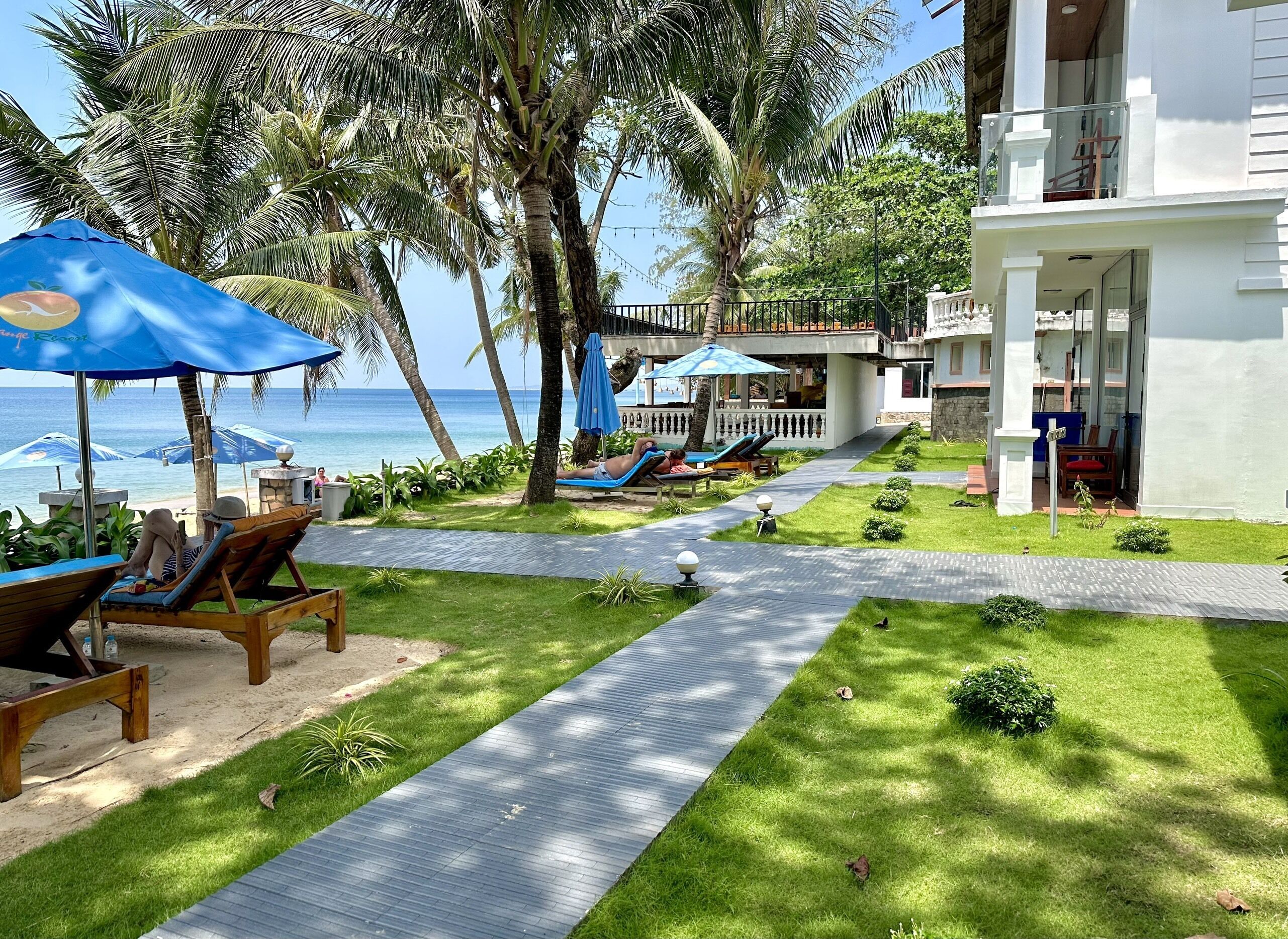 A resort with a paved walkway, lounge chairs, and umbrellas overlooking the ocean.