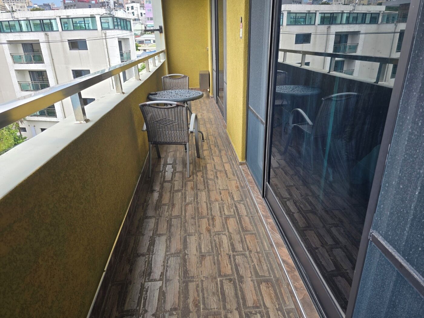 Un balcón con piso estampado, una silla de mimbre y una mesa.