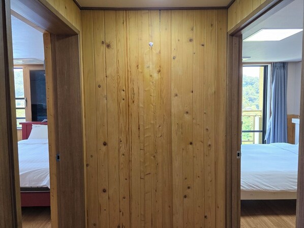 A wooden-paneled room with a bed, a red chair, and a window with curtains.