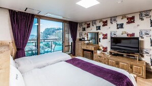 A hotel room with a large bed, a TV, wooden furniture, and a balcony with a view. - Cheonjiyeon Hotel (Seogwipo)