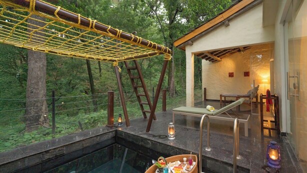 A hot tub area with a wooden swing, a lounge chair, and a basket of snacks.
