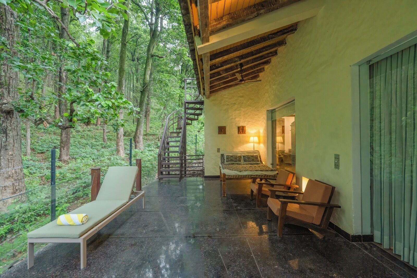 A room with a bed, a chair, a table, and a staircase leading to a balcony.