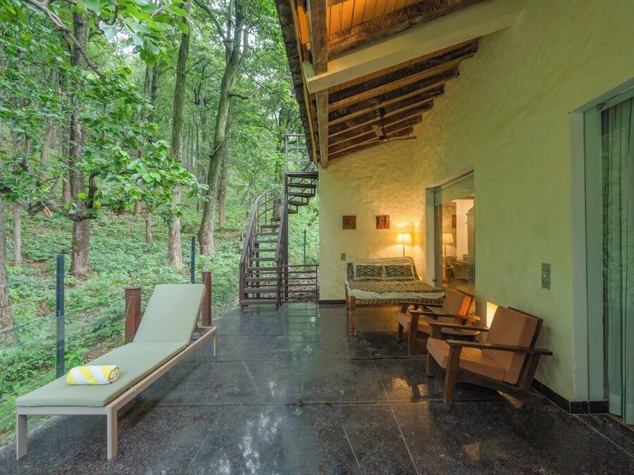 A room with a bed, a chair, a table, and a staircase leading to a balcony.