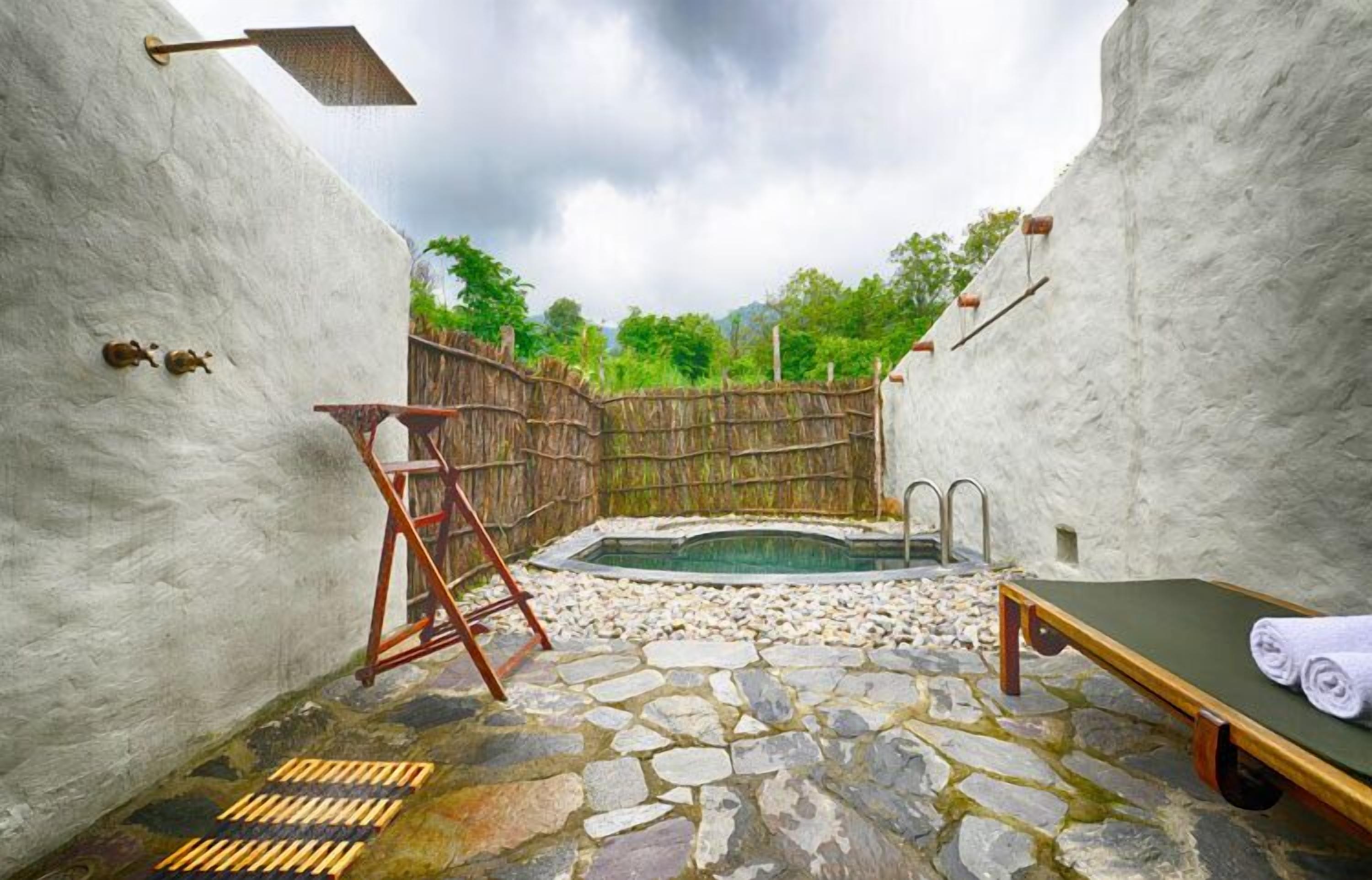 A stone-floored spa area with a small pool, a wooden ladder, a lounge chair, and a bamboo fence.