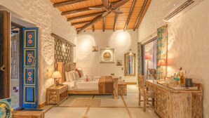 A cozy room with a bed, a wooden desk, a ceiling fan, and a stone wall.