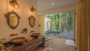 A bathroom with two large oval mirrors, a wooden vanity with a bowl sink, and a glass-enclosed outdoor shower area.