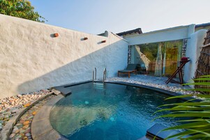 Una piscina con borde de piedra, una escalera y una silla.