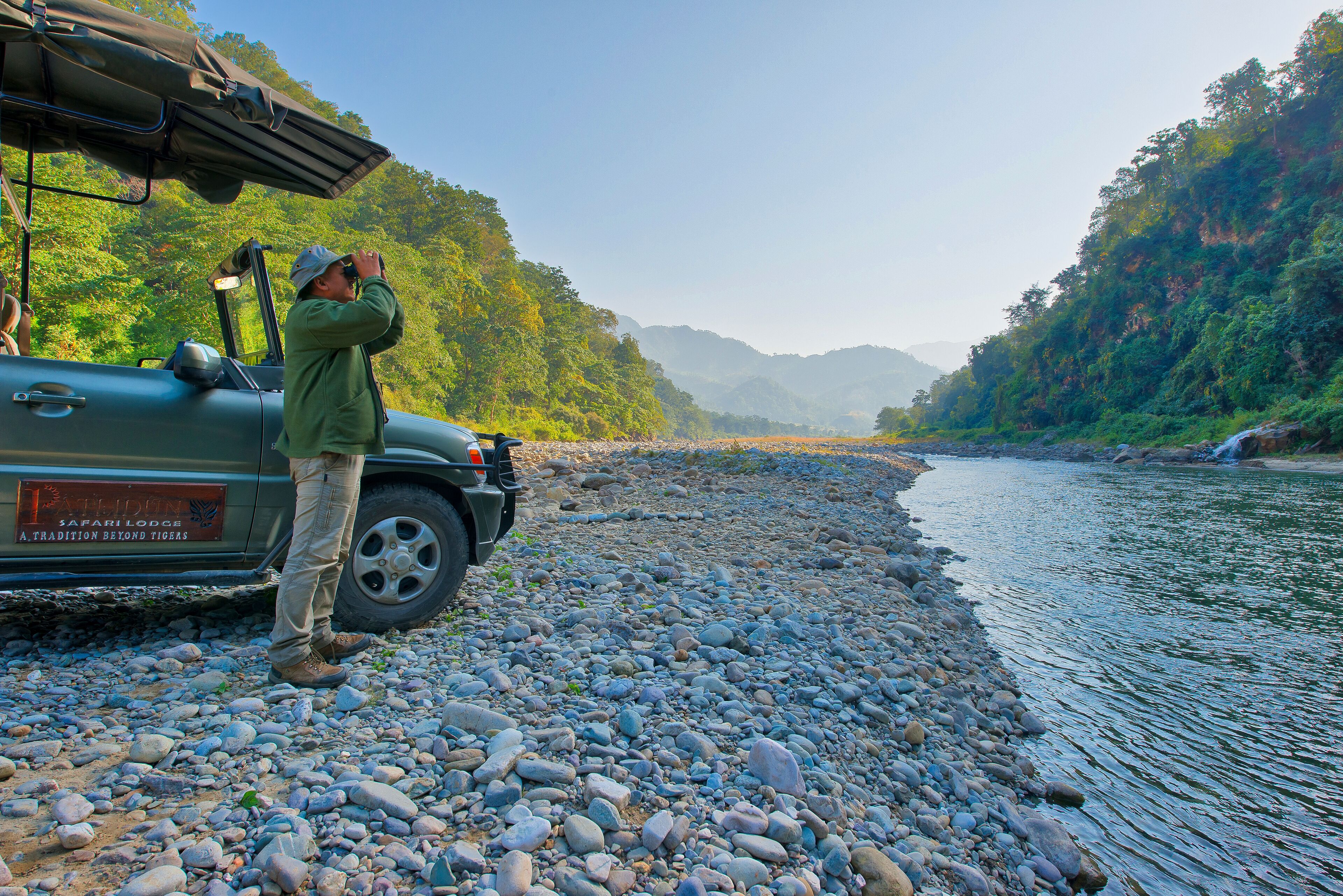 A vehicle parked by a river with a person standing beside it.