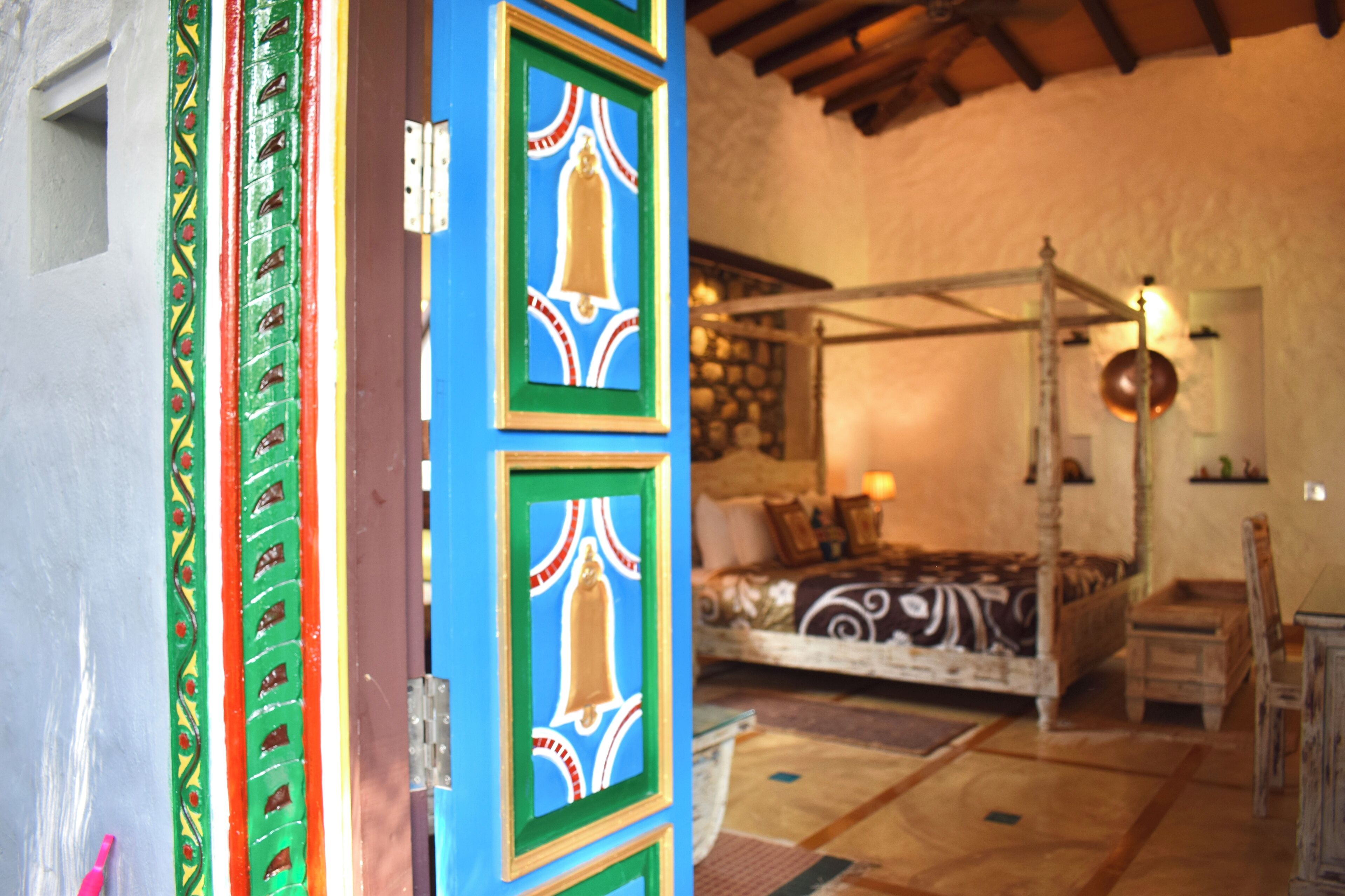 A traditional room with a four-poster bed, a wooden floor, and a colorful door.