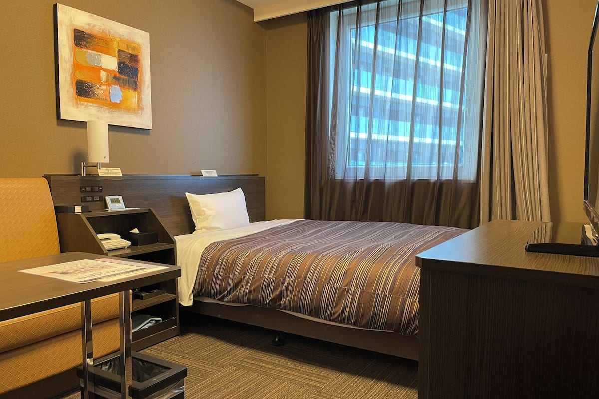 Una habitación de hotel con cama, escritorio, silla y ventana con cortinas.
