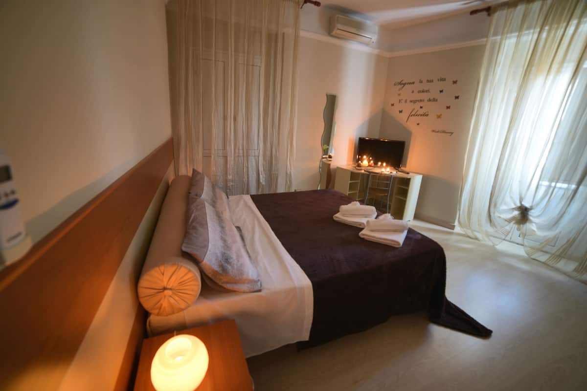 A hotel room with a bed, bedside table with a candle, a mirror, and a wall with a decorative quote.