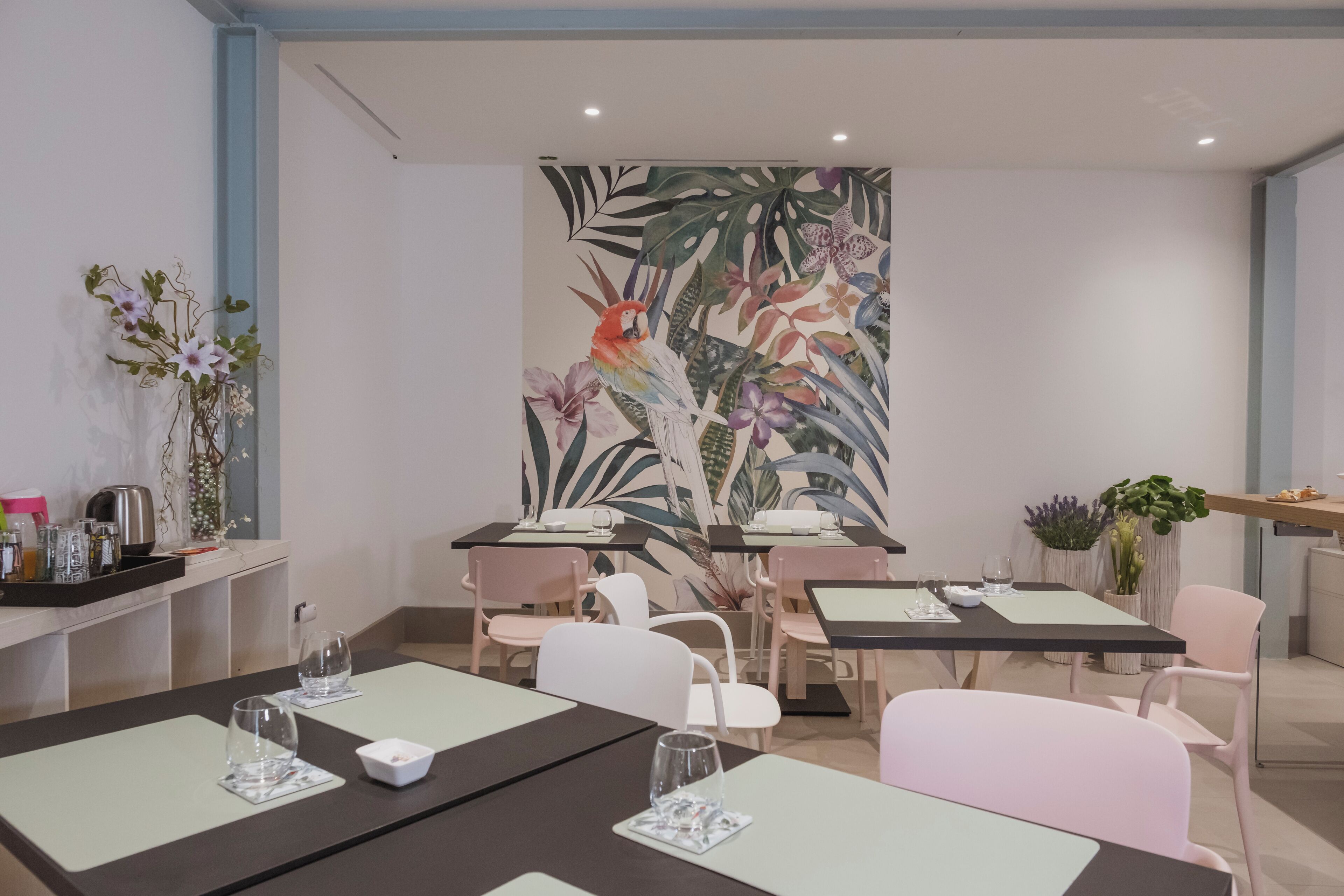 A modern dining area with tables, chairs, and a large tropical mural on the wall.